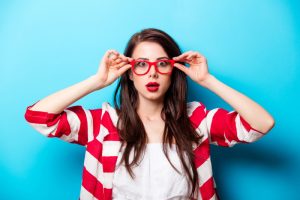 beautiful surprised young woman in glasses standing in front of wonderful blue background