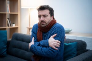 man-huddled-on-couch-with-sweater-and-scarf-looking-cold