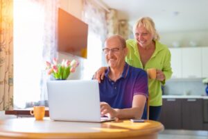 senior-couple-smiling-looking-at-laptop-at-dining-table